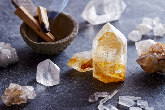 A ceramic bowl with wooden sticks and a variety of healing crystals, including a prominent yellow citrine crystal, placed on a textured surface.